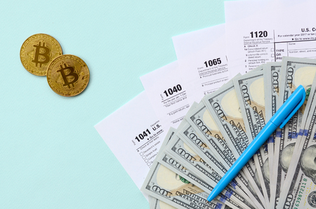 Bitcoins lies with the tax forms and hundred dollar bills on a light blue background. Income tax return.の写真素材