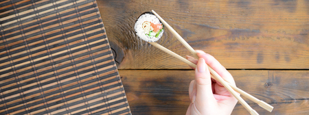 A hand with chopsticks holds a sushi roll on a bamboo straw serwing mat background. Traditional Asian food.の写真素材