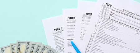 Tax forms lies near hundred dollar bills and blue pen on a light blue background. Income tax return.
