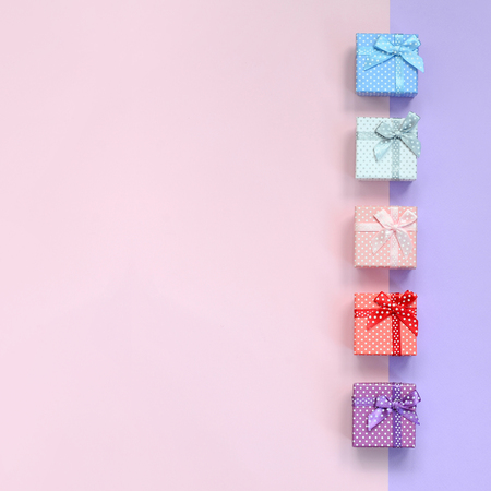 Small gift boxes of different colors with ribbons lies on a violet and pink color background.