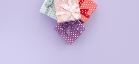 Pile of a small colored gift boxes with ribbons lies on a violet background. Minimalism flat lay top...