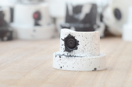 Several plastic nozzles from a paint sprayer that lie on a wooden surface against a gray wall background. The caps are smeared in black paint. The concept of street art and graffitiの写真素材