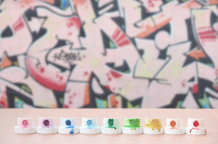 The soiled multicolored nozzles from the paint sprayer are lined up on a wooden table on a background of colored graffiti drawing in a wild style. The concept of street artの写真素材