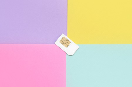 Subscriber identity module. New white SIM card on bright multicolor background. Minimal flat lay top view. Violet, pink, yellow and blue pastel colorsの写真素材