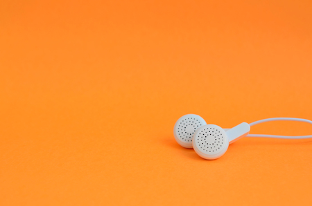 White modern headphones lie on a bright orange background. A template for music listening fansの写真素材