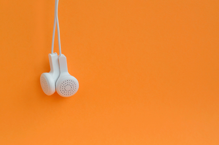White modern headphones hanging on a bright orange background. A template for music listening fansの写真素材