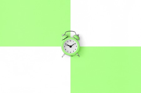 A small green alarm clock is located between areas of green and white colors. Time management concept. Flat lay minimal template with copy space. Top viewの写真素材