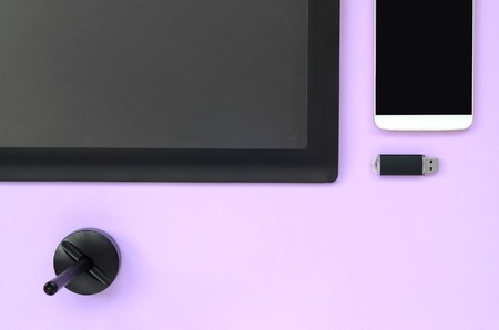Graphic tablet and pen for illustrators and designers lies with USB memory card and smartphone on pastel violet background. Flat lay minimalism. Top viewの写真素材