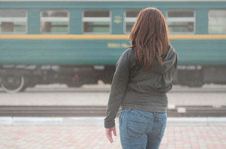 A young red-haired girl is standing on the railway platform and watching the departing train. The woman was late for her train. Back viewの写真素材
