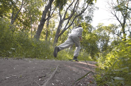 A young guy in a gray sports suit runs along the path among the trees in the forest. Sports jogging...