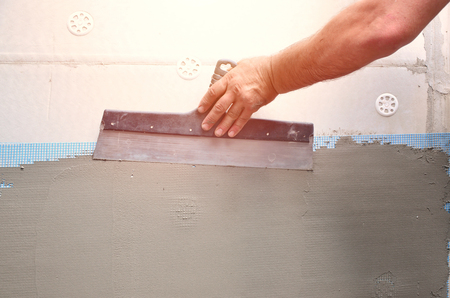 Hands of an old manual worker with wall plastering tools renovating house. Plasterer renovating outdoor walls and corners with spatula and plaster. Wall insulation. Construction finishing worksの写真素材