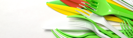 Pile of bright yellow, green and white plastic kitchenware single use appliances on white background