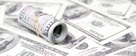 US dollars rolled up and tightened with band lies on a lot of american banknotes with blurred...