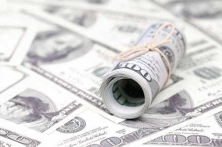 US dollars rolled up and tightened with band lies on a lot of american banknotes with blurred...