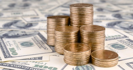 Stack of ukrainian coins in rising stacks grow up. Ukrainian money lies on US hundred dollar bills
