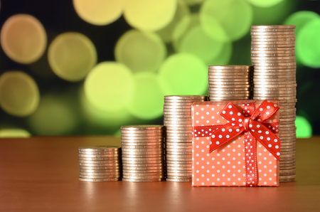 Small red gift box and golden coin stacks on the colored bokeh background. Special offer or cashback conceptの写真素材