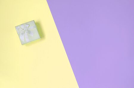 Small yellow gift box lie on texture background of fashion pastel yellow and violet colors paper in minimal concept.の写真素材