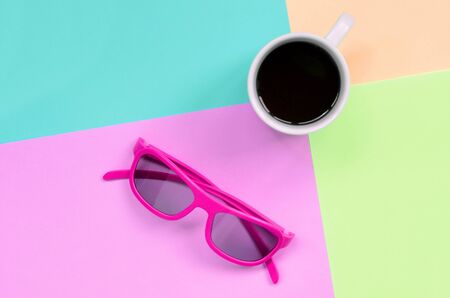 Small white coffee cup and pink sunglasses on texture background of fashion pastel pink, blue, coral and lime colors paper in minimal concept.の写真素材
