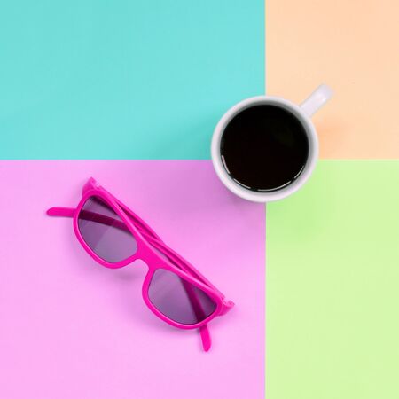 Small white coffee cup and pink sunglasses on texture background of fashion pastel pink, blue, coral and lime colors paper in minimal concept.の写真素材