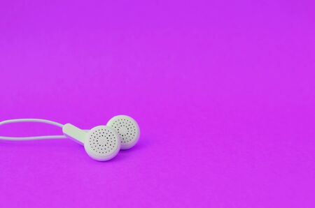 White modern headphones lie on a bright purple background. A template for music listening fans