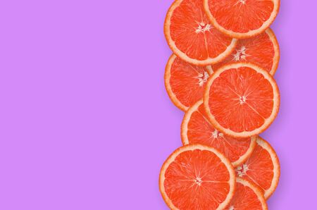 Top view of grapefruit fruit slices on bright purple background. A saturated citrus vertical row with copy space. Minimalistic flat layの写真素材