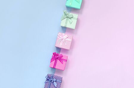 Small gift boxes of different colors with ribbons lies on a violet and pink color background.の写真素材