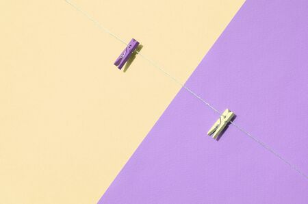 Two colored wooden pegs and small rope lie on texture background of fashion pastel yellow and violet...