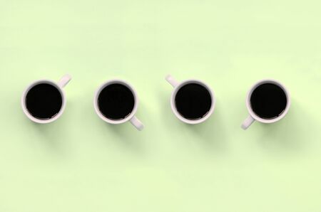 Many small white coffee cups on texture background of fashion pastel lime color paper in minimal...