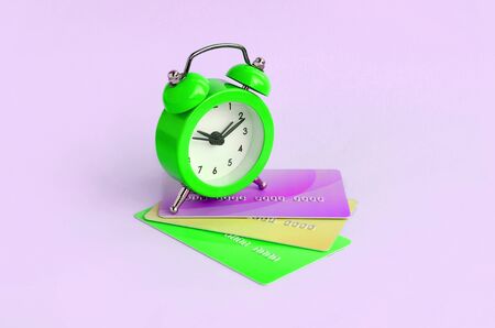 Small green alarm clock lies on colored credit cards. The concept of modern fast online banking and funds transfer operationsの写真素材