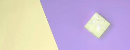 Small yellow gift box lie on texture background of fashion pastel yellow and violet colors paper in minimal concept.の写真素材