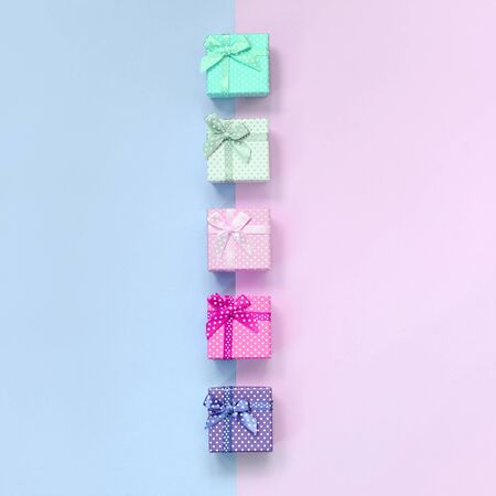 Small gift boxes of different colors with ribbons lies on a violet and pink color background.の写真素材