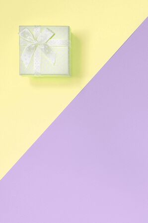 Small yellow gift box lie on texture background of fashion pastel yellow and violet colors paper in minimal concept.の写真素材