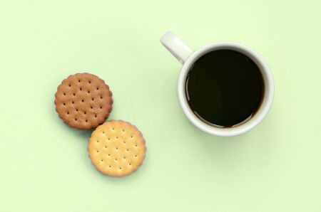 Coffee break flat lay composition with brown sandwich cookies. White hot coffee cup and brown dessert on a trendy pastel lime backgroundの写真素材