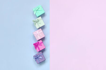 Small gift boxes of different colors with ribbons lies on a violet and pink color background.の写真素材