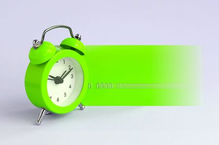 Small green alarm clock is next to green credit card in motion. The concept of modern fast online banking and instant financial operationsの写真素材