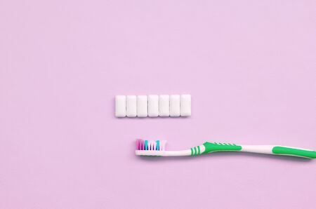 Toothbrush and chewing gums lie on a pastel pink background. Top view, flat lay. Minimal concept.