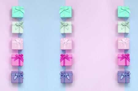 Small gift boxes of different colors with ribbons lies on a violet and pink color background.の写真素材