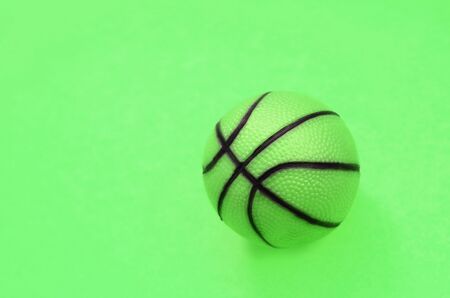 Small green ball for basketball sport game lies on texture background of fashion pastel green color...