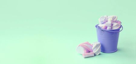 A miniature lilac bucket filled with marshmallow lies on a green pastel background. Minimal concept.の写真素材