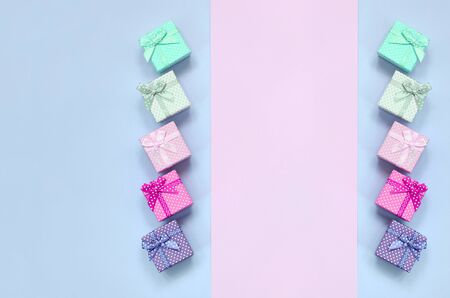 Small gift boxes of different colors with ribbons lies on a violet and pink color background.の写真素材