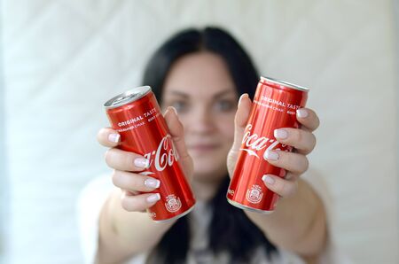 KHARKIV, UKRAINE - JULY 15, 2019: Happy woman holding two non-alcoholic Coca-Cola aluminium tin cans...