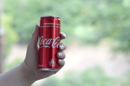 KHARKIV, UKRAINE - JULY 15, 2019: Caucasian woman holds red Coca-Cola tin can with green garden...