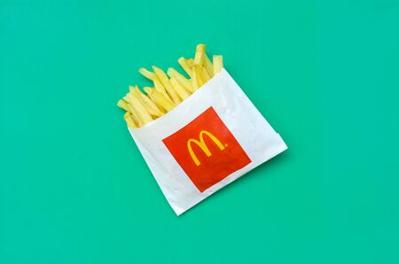 KHARKIV, UKRAINE - AUGUST 1, 2019: McDonald's French fries in small paperbag on bright green background. McDonald's Corporation is the world's largest and famous fast food restaurantのeditorial素材