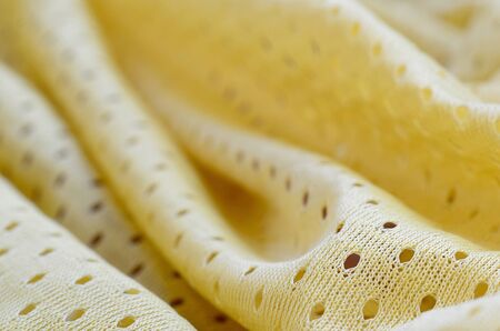 Yellow mesh sport wear fabric textile pattern background. Yellow color football jersey clothing fabric texture sports wear. Breathable porous poriferous material air ventilation with small holesの写真素材