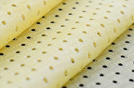 Yellow mesh sport wear fabric textile pattern background. Yellow color football jersey clothing fabric texture sports wear. Breathable porous poriferous material air ventilation with small holesの写真素材