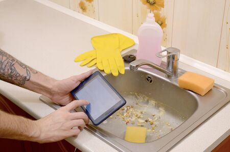 The landlord uses the tablet to call a cleaner in order to clean the clogged kitchen sink. A man turned in to internet searchの写真素材