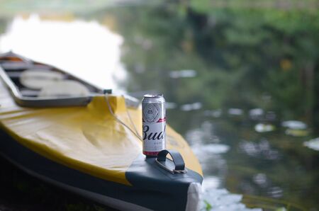 SUMY, UKRAINE - AUGUST 10, 2019: Budweiser Bud beer can on yellow kayak outdoors in the river and green trees blurred background. Budweiser is one of the most popular domestic brands in the United Statesのeditorial素材