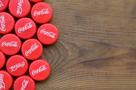KHARKOV, UKRAINE - SEPTEMBER 8, 2019: Many red caps with coca cola logo on wooden background. The Coca-Cola is a non alcoholic world famous beverage drinkのeditorial素材