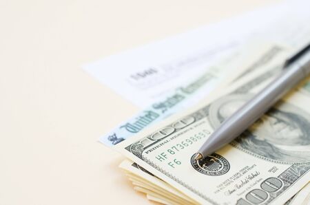1040 Individual Income tax return form with Refund Check and hundred dollar bills on beige...