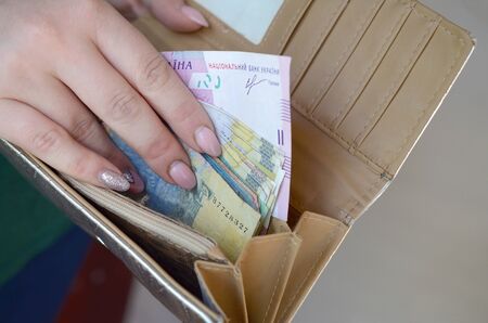 Female hands holding ukrainian hryvnia bills in small money pouch or wallet. Small salary in...